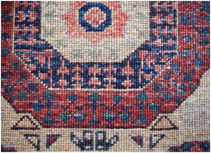 A close-up of a handmade Afghan Chobi runner featuring a geometric medallion in red and blue.