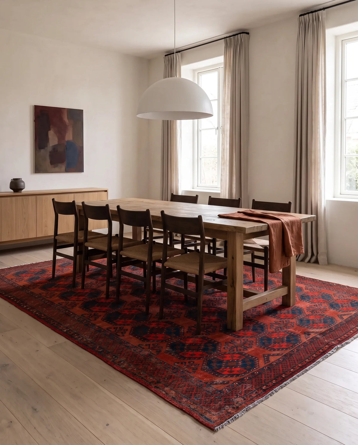 Antique Turkmen Ersari rug with red and blue elephant's foot guls, styled under a wooden dining table in a bright room.