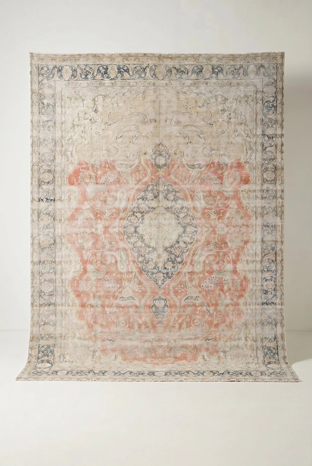Vintage Persian Kerman rug with a faded coral and blue floral medallion pattern on a neutral wool and cotton field.