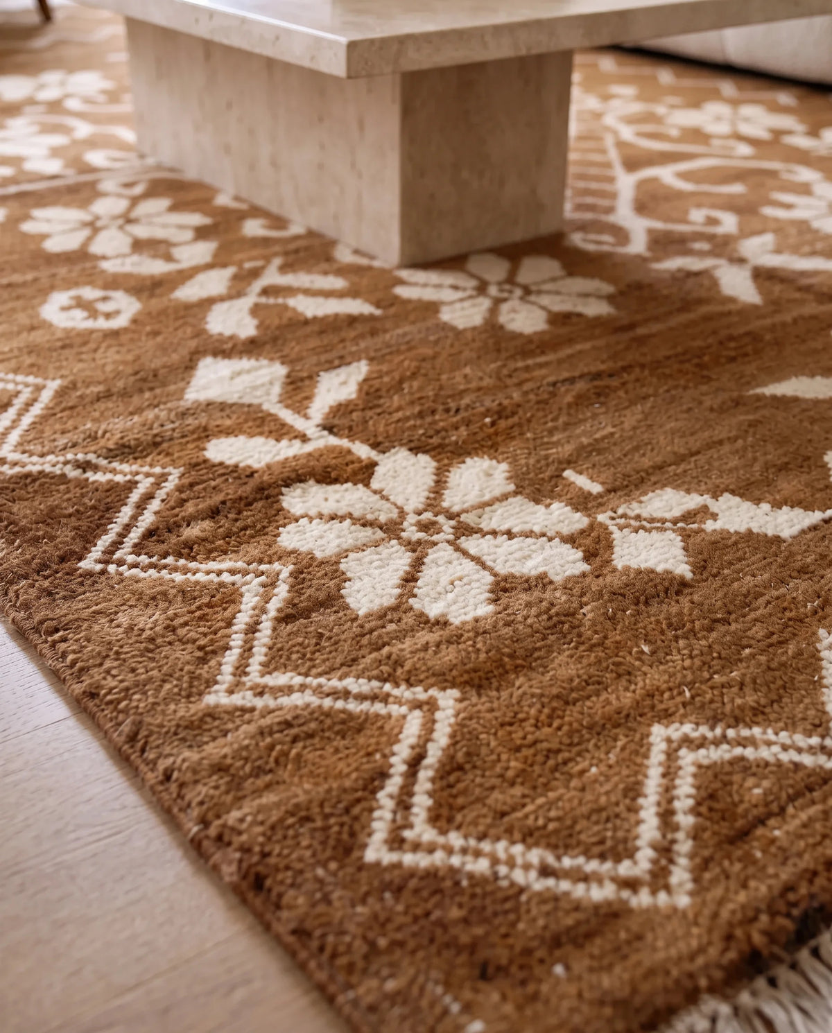 Close-up of a hand-knotted Afghan wool rug featuring a brown and cream floral pattern with geometric zigzag borders.