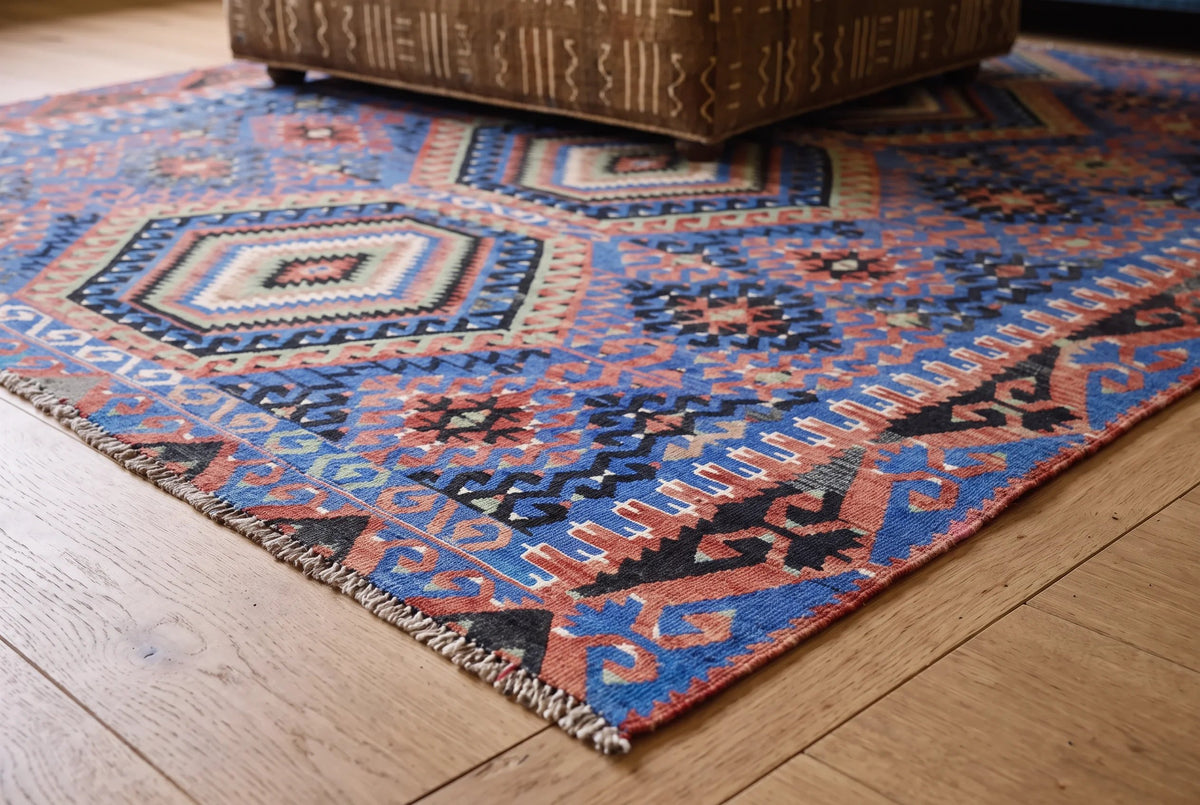 Vintage Anatolian kilim with blue, red, and geometric diamond patterns on a timber floor.