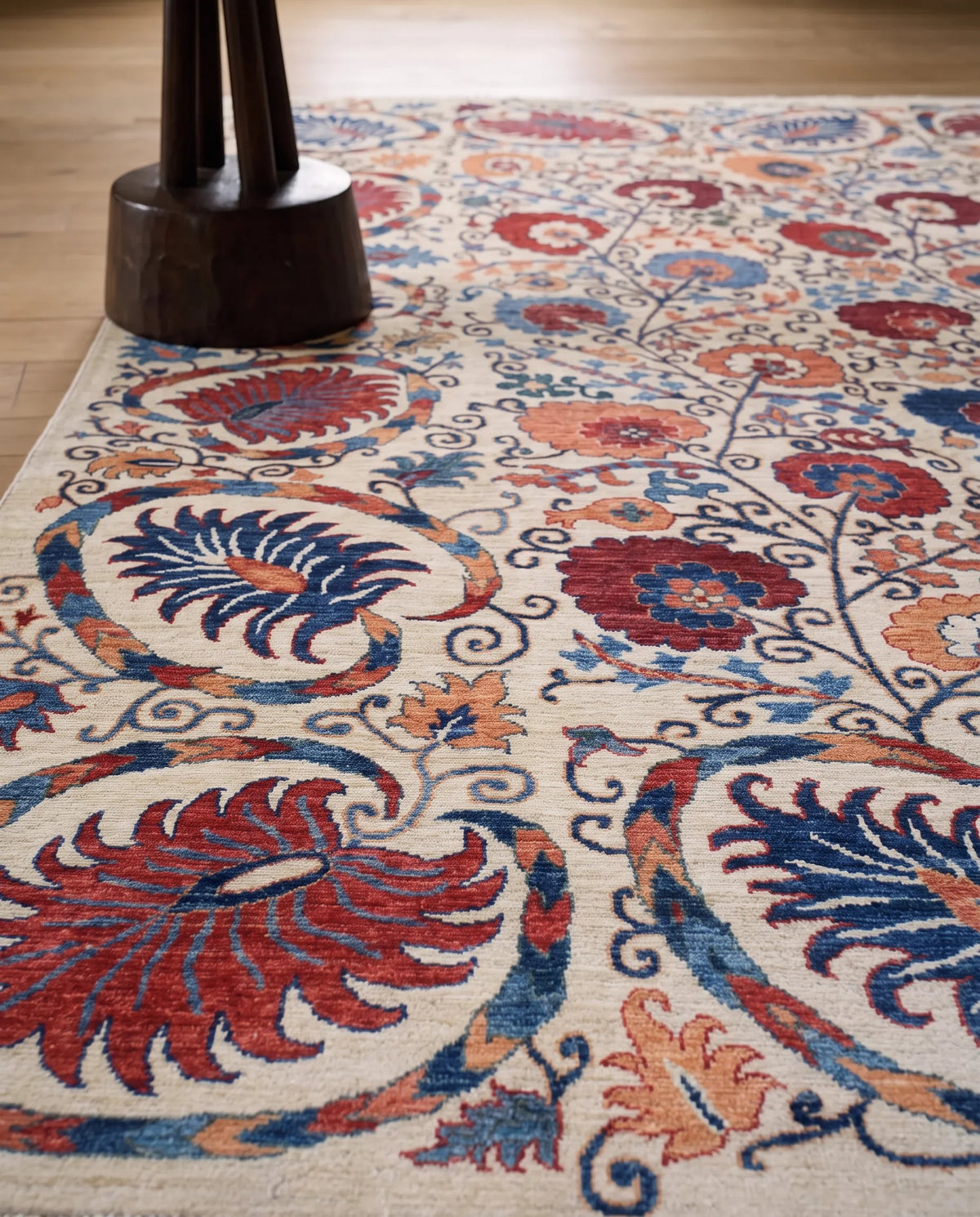 Hand-knotted Afghan Chobi rug with a cream base and intricate floral patterns in red, blue, and orange on a timber floor.