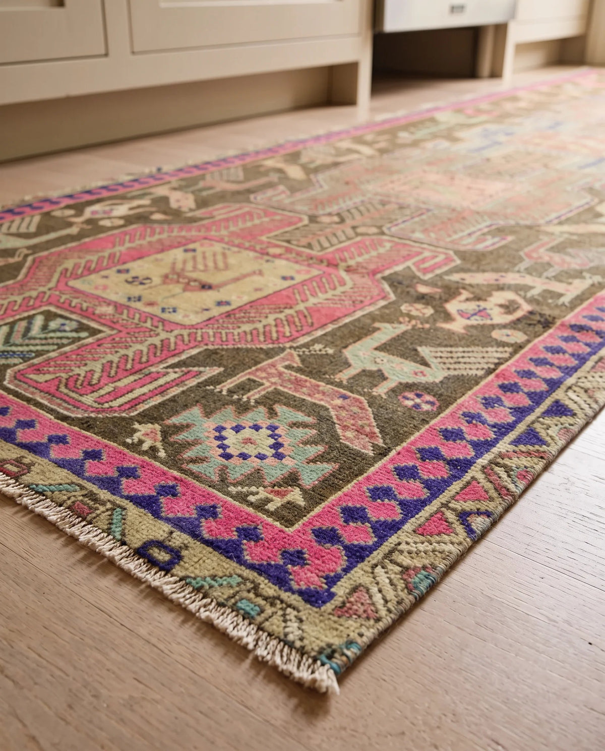 Vintage Persian Ardabil wool runner featuring pink, blue, and brown geometric motifs with a fringed edge on timber flooring.
