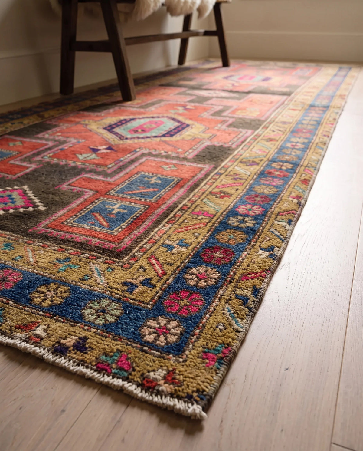Vintage Persian Meshkin runner with geometric medallions in red, blue, and gold on a light timber floor.