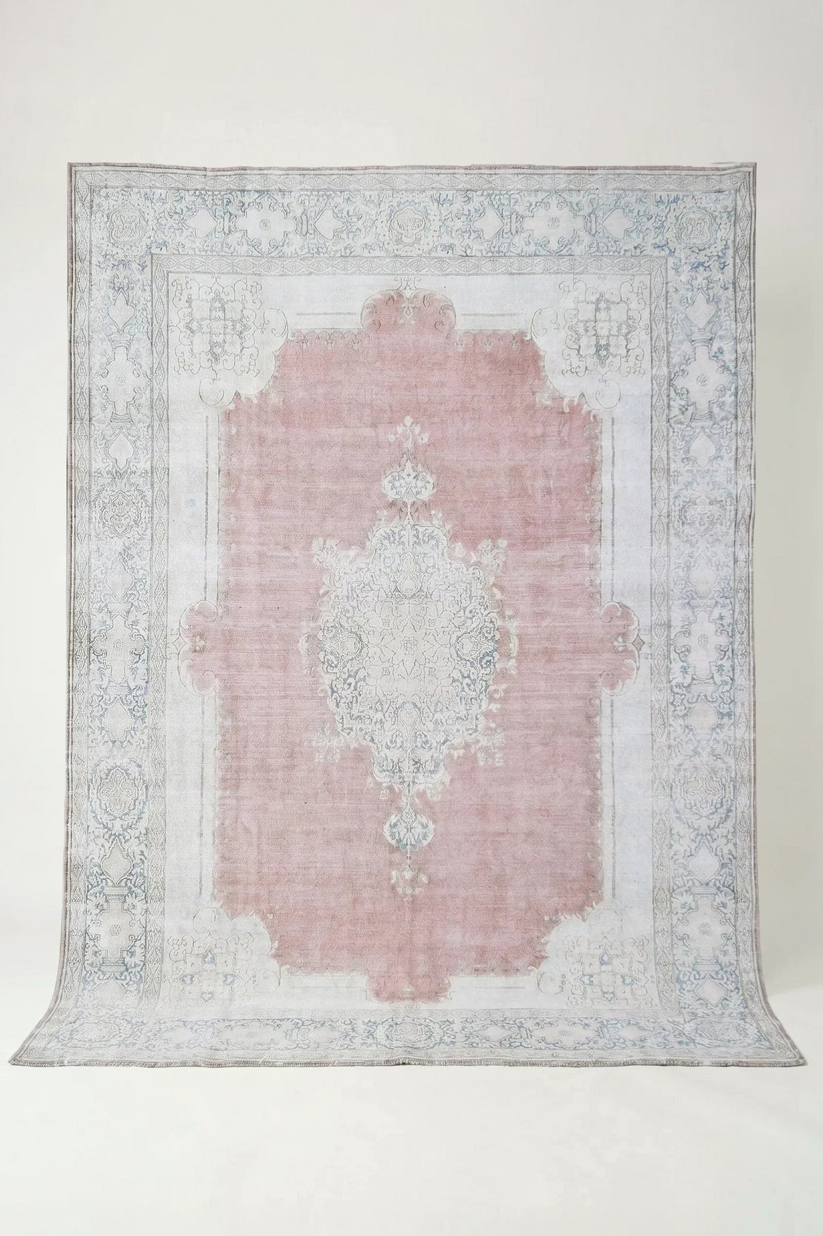 Vintage Persian Kerman wool rug featuring a dusty pink field, intricate cream central medallion, and ornate floral borders.