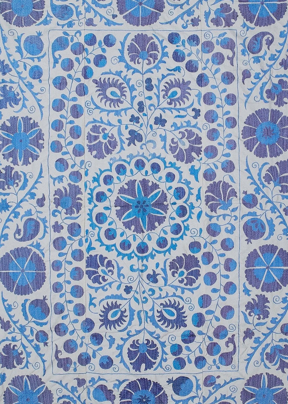 Hand-embroidered Uzbek Suzani textile featuring intricate blue and purple floral and pomegranate motifs on cotton.