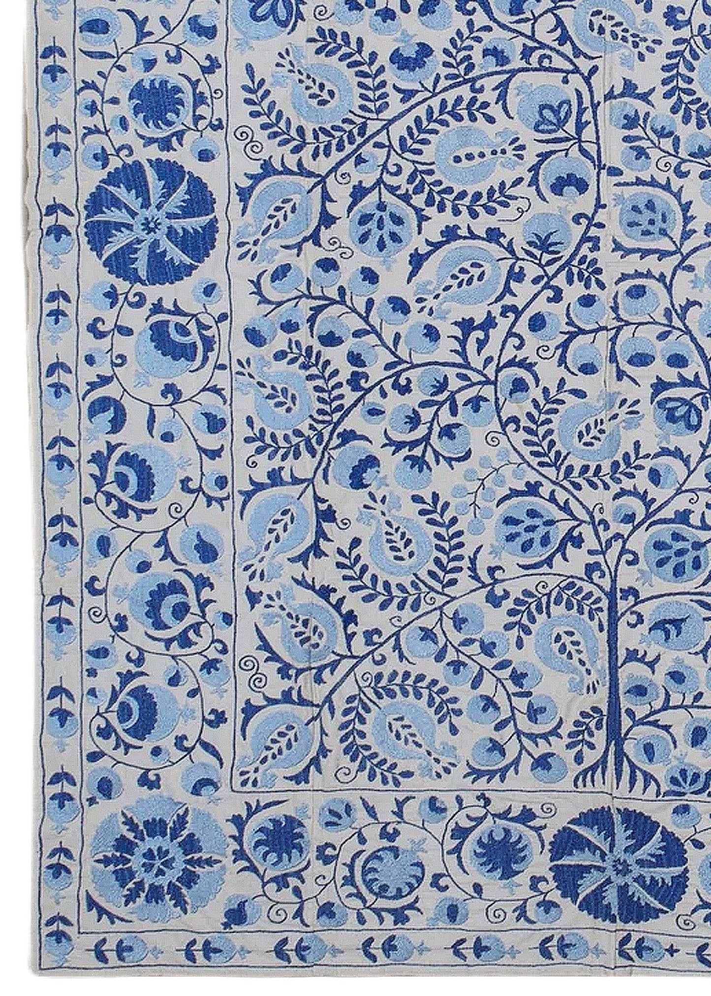 An Uzbek Suzani textile featuring intricate blue floral and pomegranate embroidery on a light base.