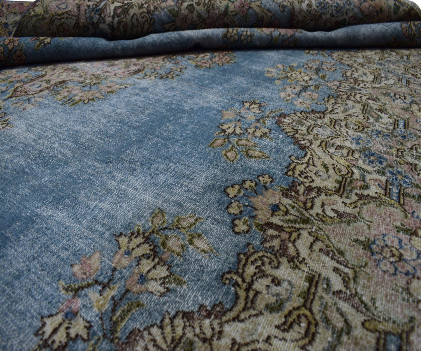 A vintage Persian Kerman rug featuring intricate floral patterns on a faded blue field.