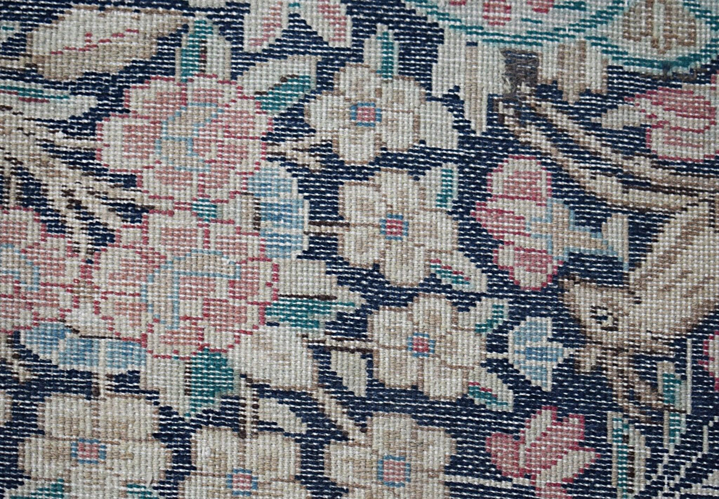 A close-up of a vintage Persian Kerman rug featuring intricate floral patterns on a dark blue field.