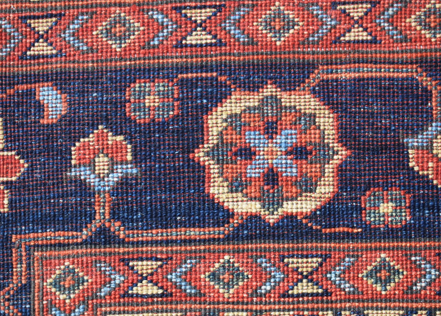 A close-up of an Afghan Chobi rug featuring intricate geometric and floral patterns in red and blue.