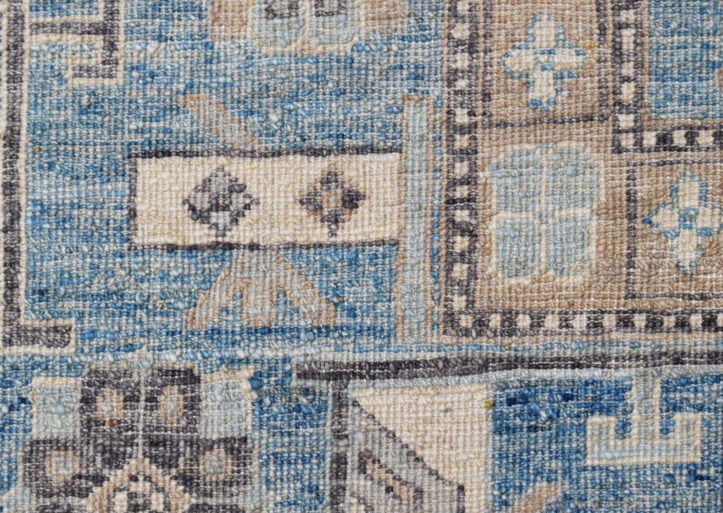 A close-up of a handwoven Afghan Chobi rug featuring geometric patterns in blue and beige tones.