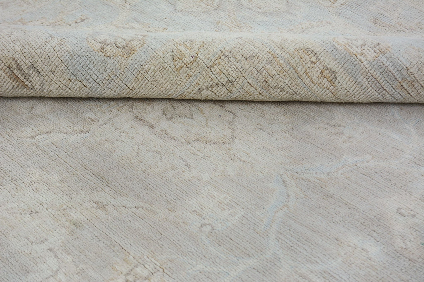 A close-up of a handmade Afghan Chobi rug in neutral tones with a folded corner.