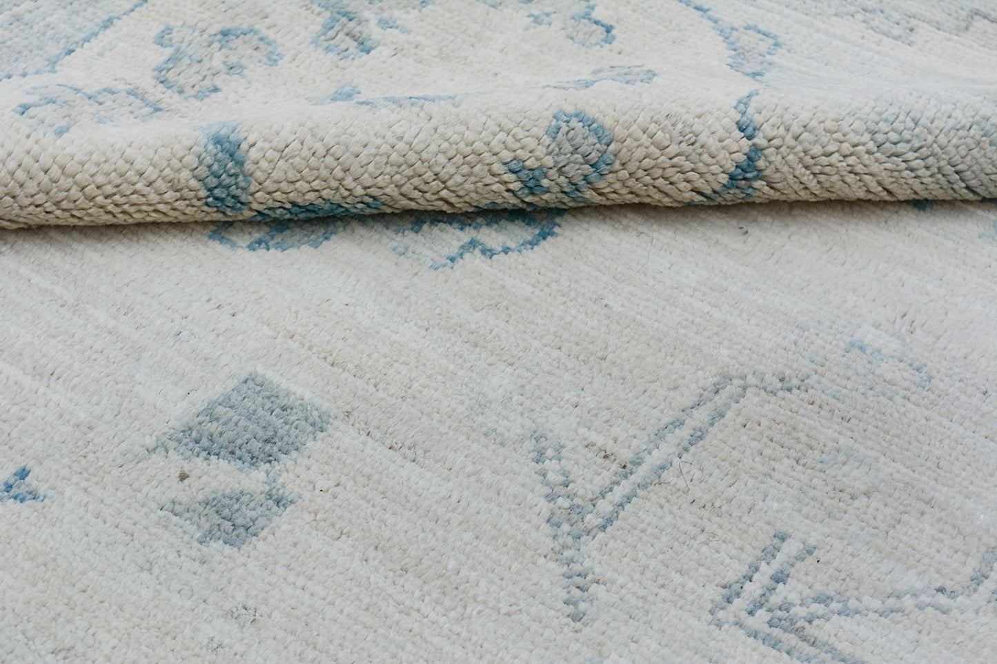 A handmade Afghan Chobi rug featuring a cream wool pile with a soft blue floral pattern.