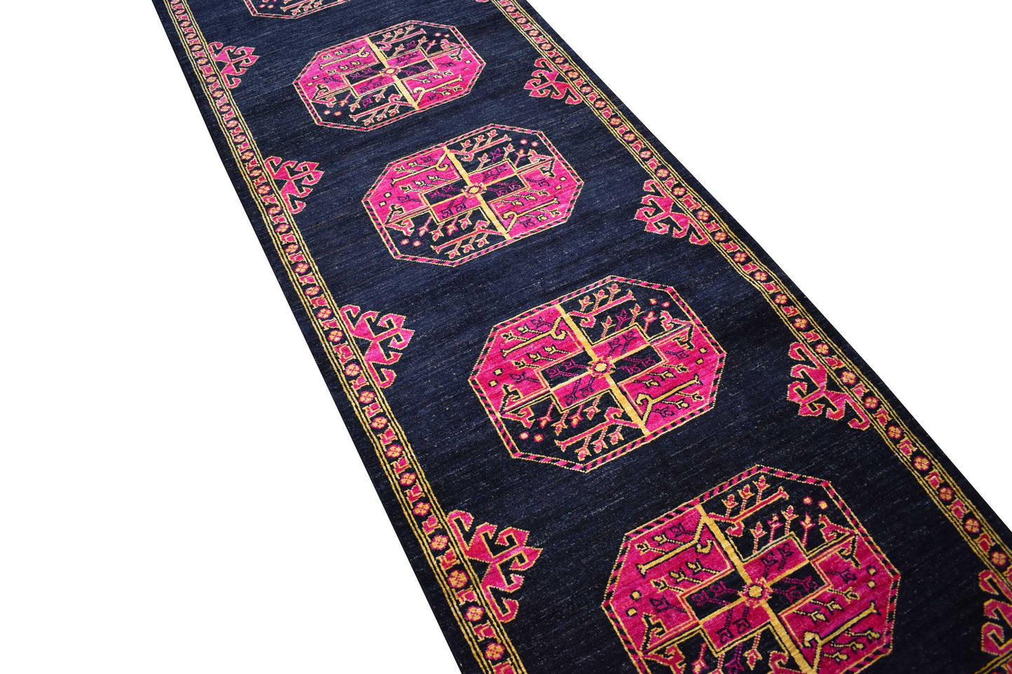 A handmade Afghan Chobi runner rug featuring pink and gold geometric motifs on a dark blue field.