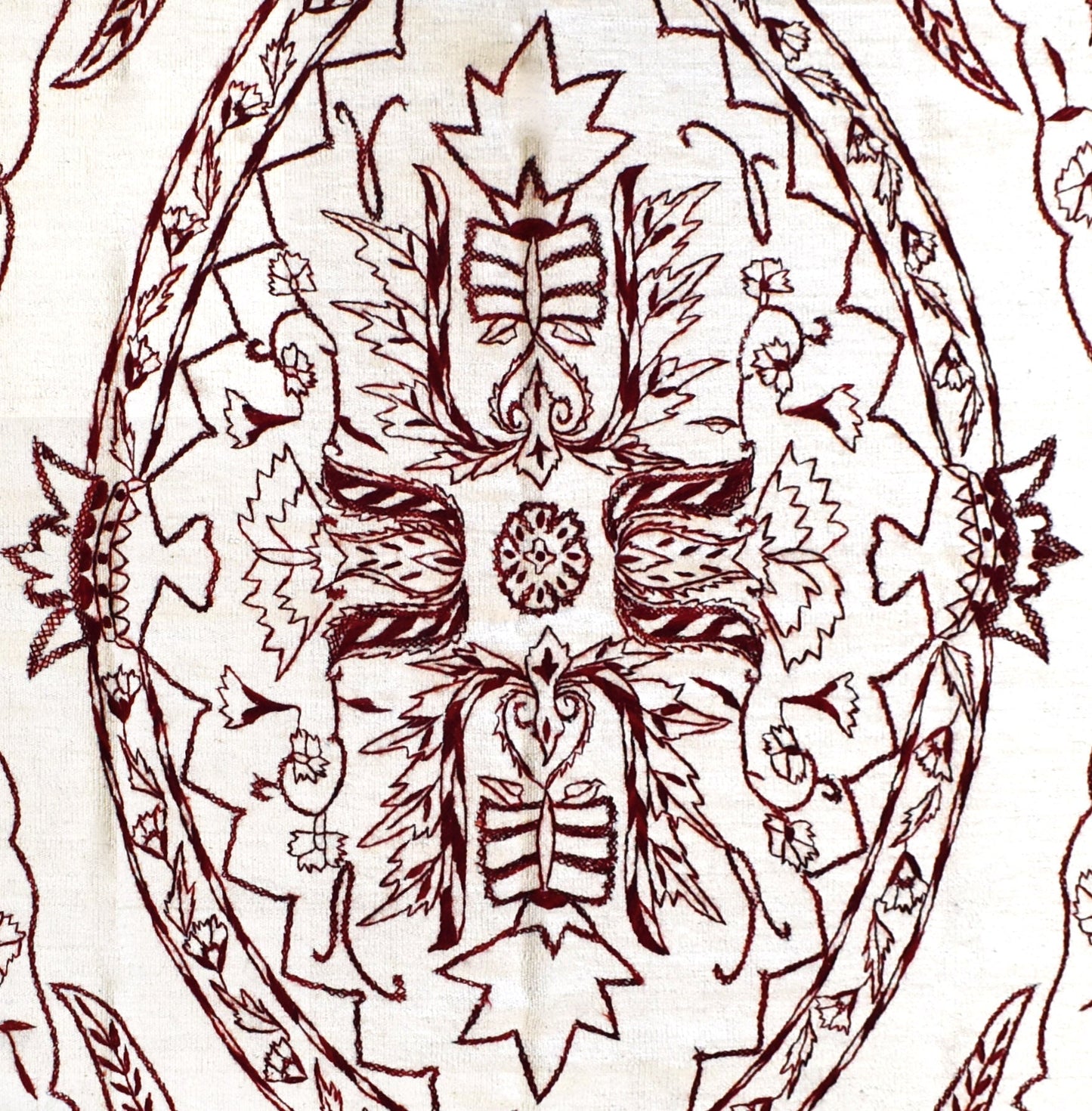 A close-up of an Afghan kilim featuring intricate dark red hand-embroidered floral motifs.