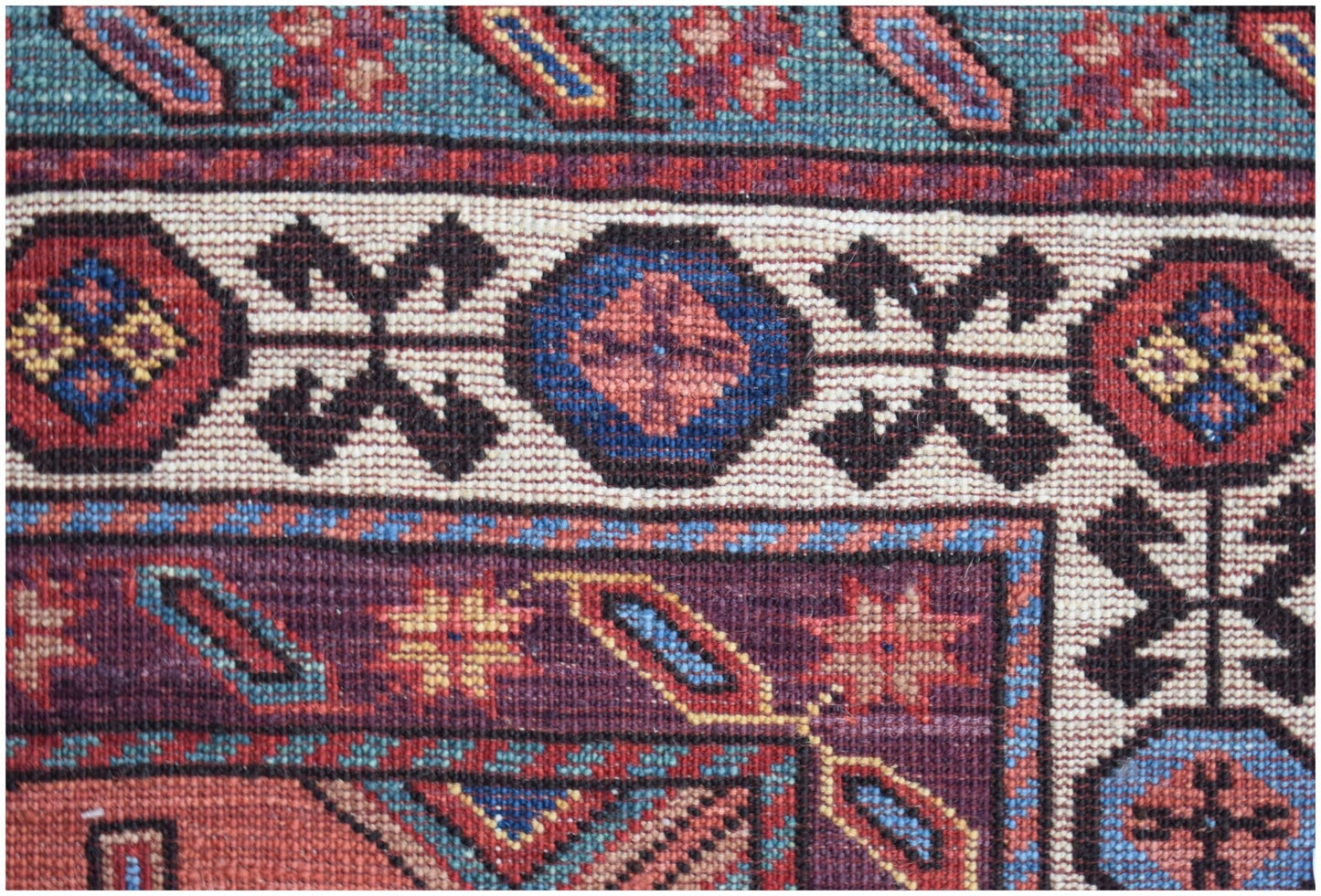 A close-up of an Afghan Herati rug featuring intricate geometric patterns in red, blue, and cream.