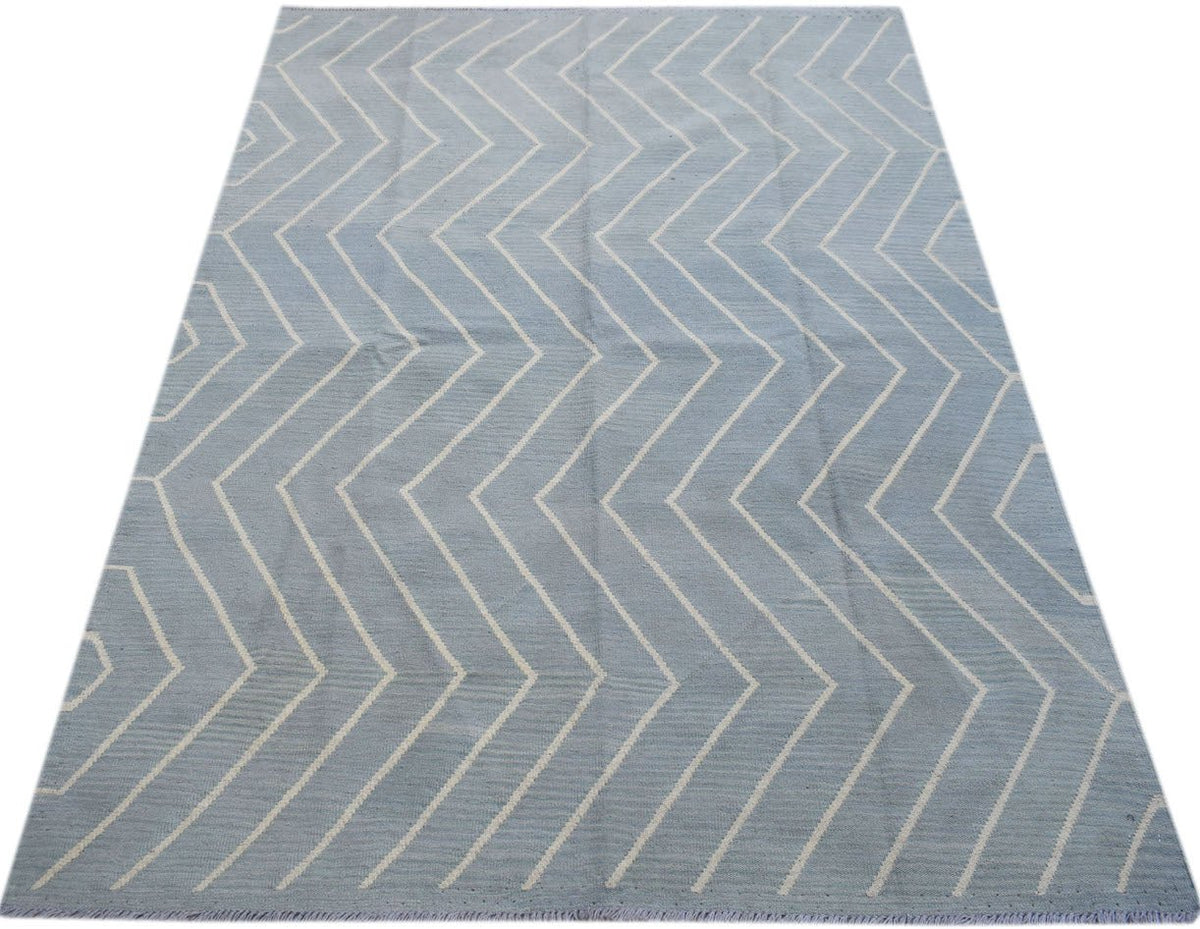 A handmade Afghan Maimana kilim rug featuring a light blue field with a white chevron pattern.