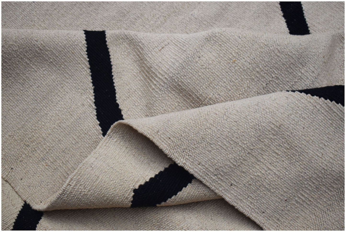 A handmade Afghan Maimana kilim featuring a minimalist black striped pattern on a cream wool base.