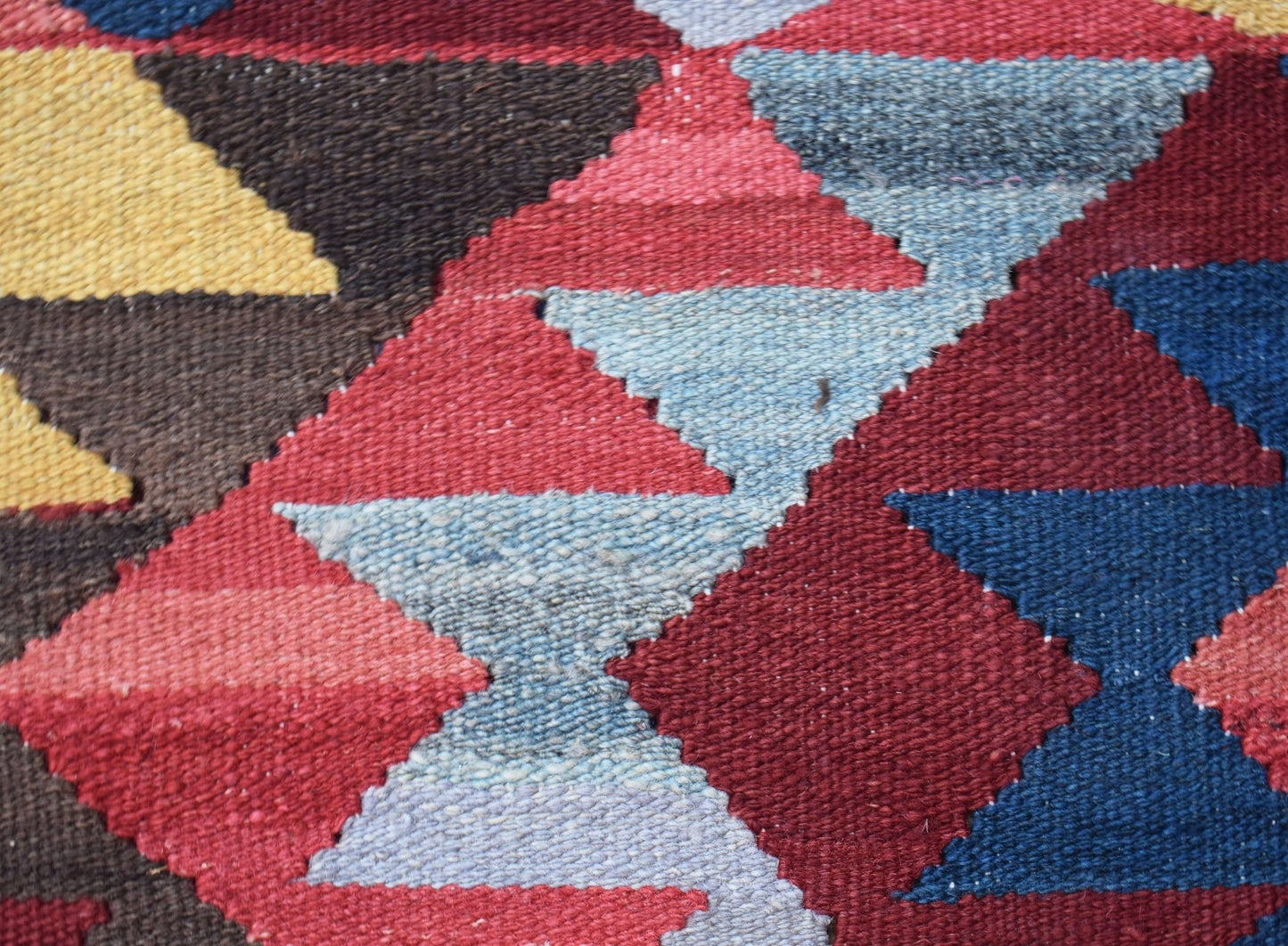 A close-up of a handmade Afghan Maimana kilim featuring a geometric pattern in red, blue, and gold.