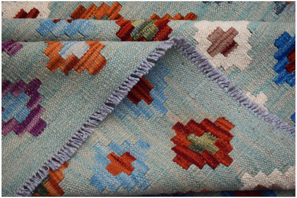 A handwoven Afghan Maimana kilim rug featuring a light blue background with colorful geometric motifs.