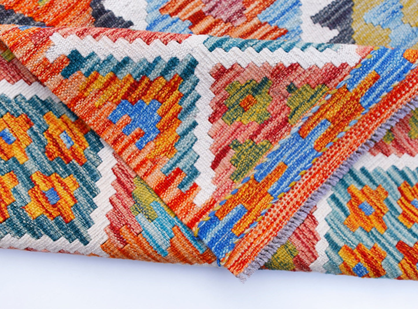 A folded Afghan Maimana kilim rug featuring vibrant geometric patterns in wool.