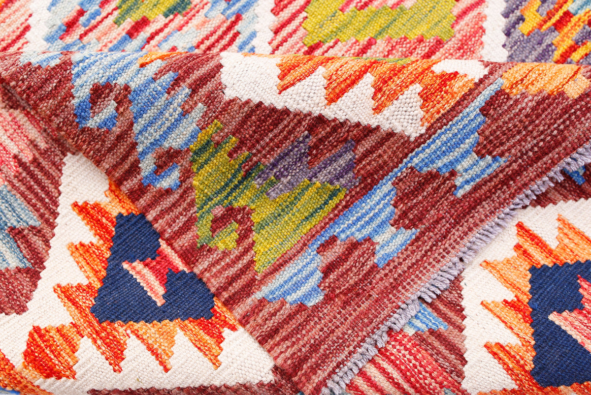 A folded handmade Afghan Maimana kilim rug featuring vibrant geometric patterns in wool.