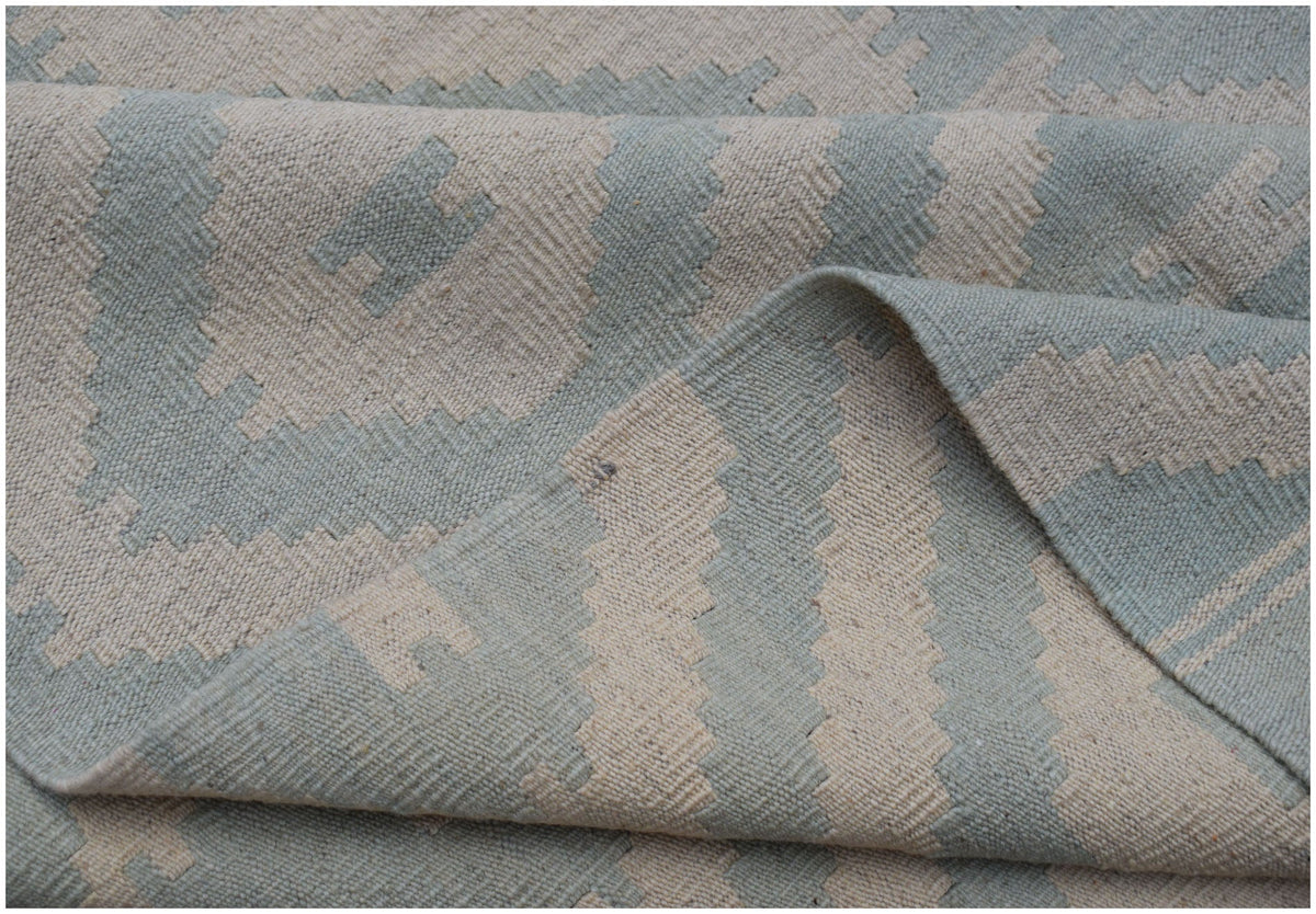 A handwoven Afghan Maimana kilim rug featuring a geometric pattern in light blue and cream wool.