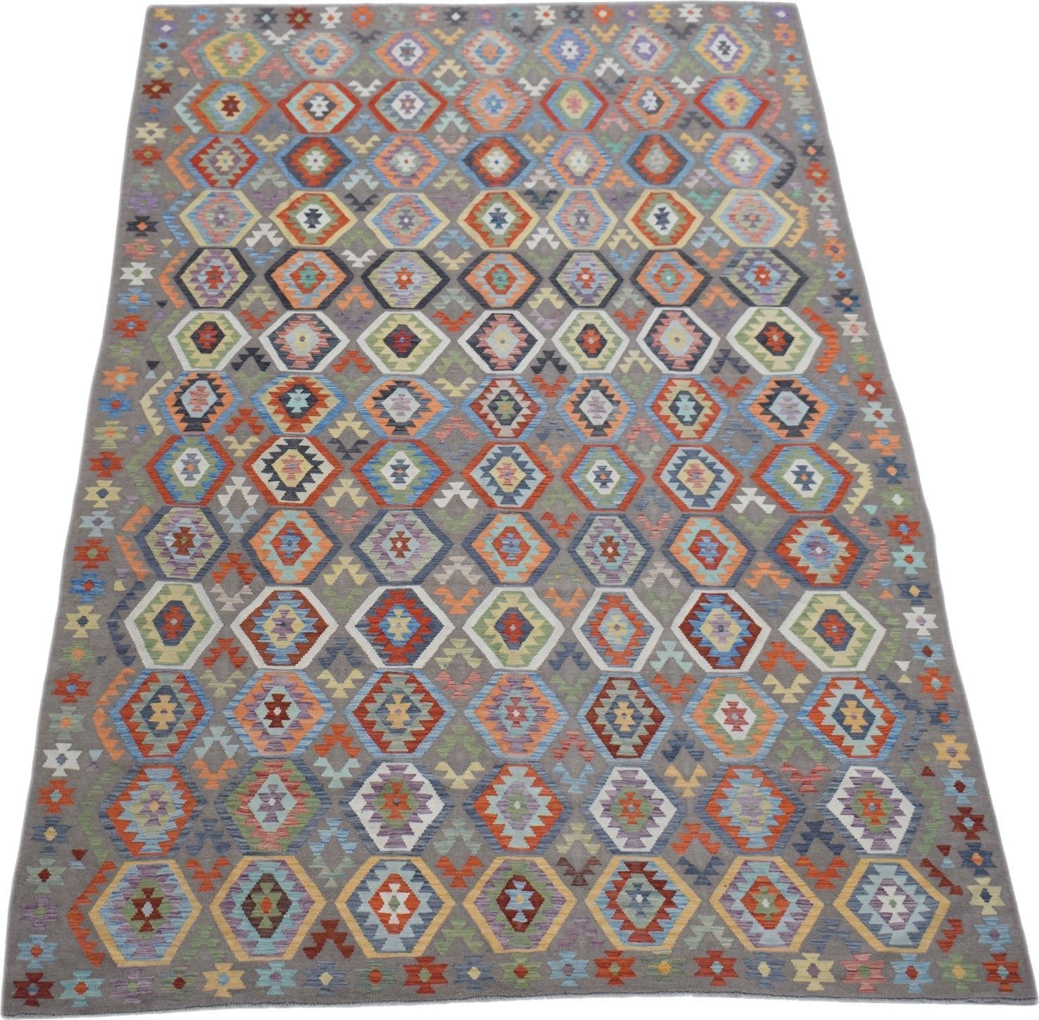 Handwoven Afghan Maimana kilim rug featuring a colorful geometric pattern on a grey background.