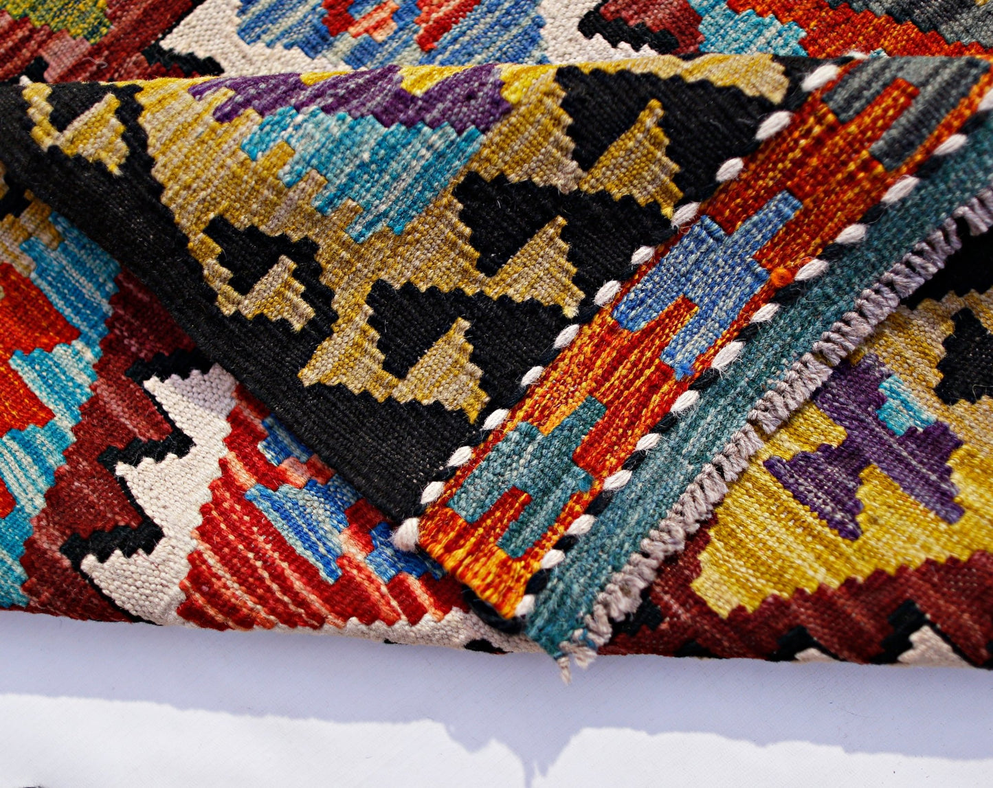 A folded Afghan Maimana kilim runner featuring vibrant geometric patterns in wool.