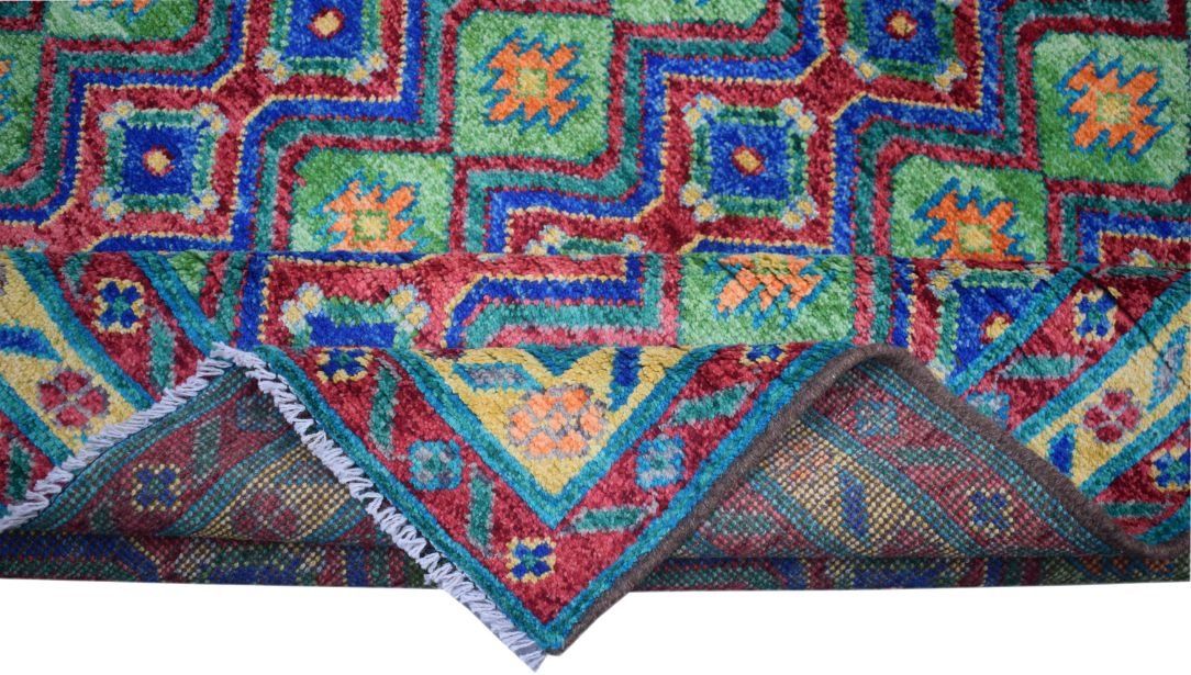 A handmade Afghan Pashm wool rug featuring a vibrant geometric pattern in red, green, and blue.