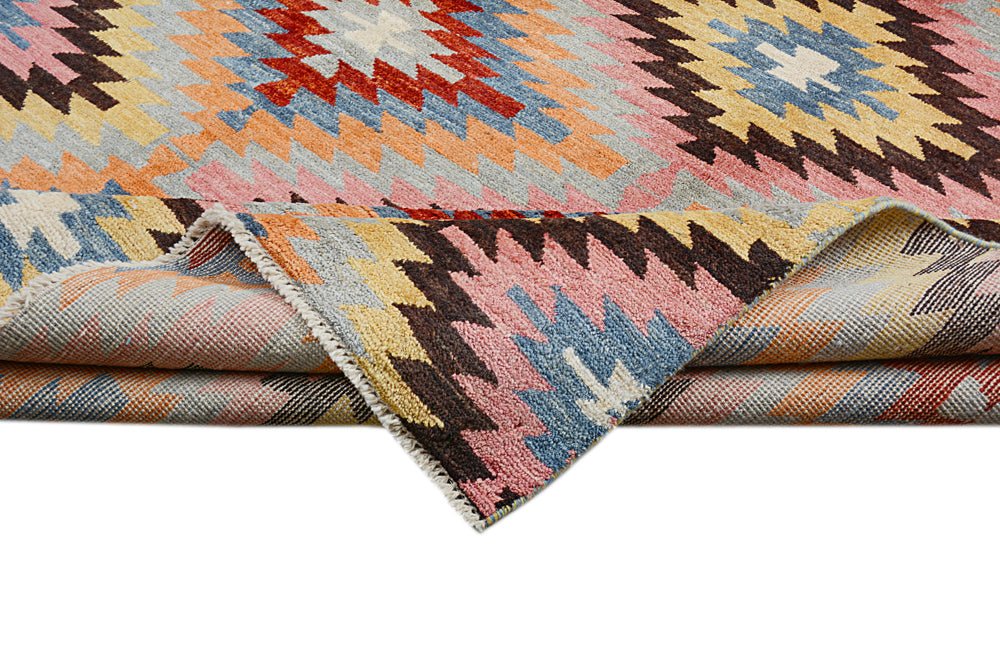 Handmade Afghan wool rug featuring a colorful geometric kilim pattern with a folded corner.