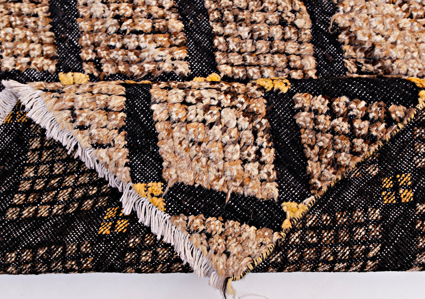 An Afghan Yekta rug featuring a black and tan geometric pattern with a textured pile and fringe.