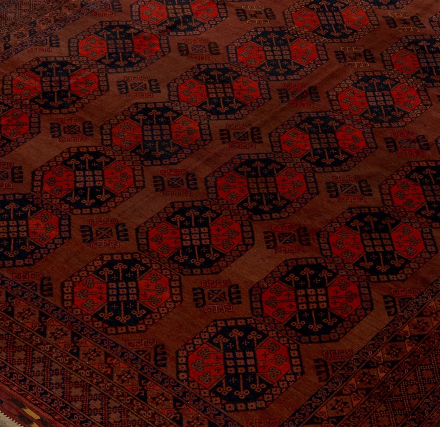 An antique Afghan Turkmen rug featuring a repeating geometric gul pattern in red and dark blue.