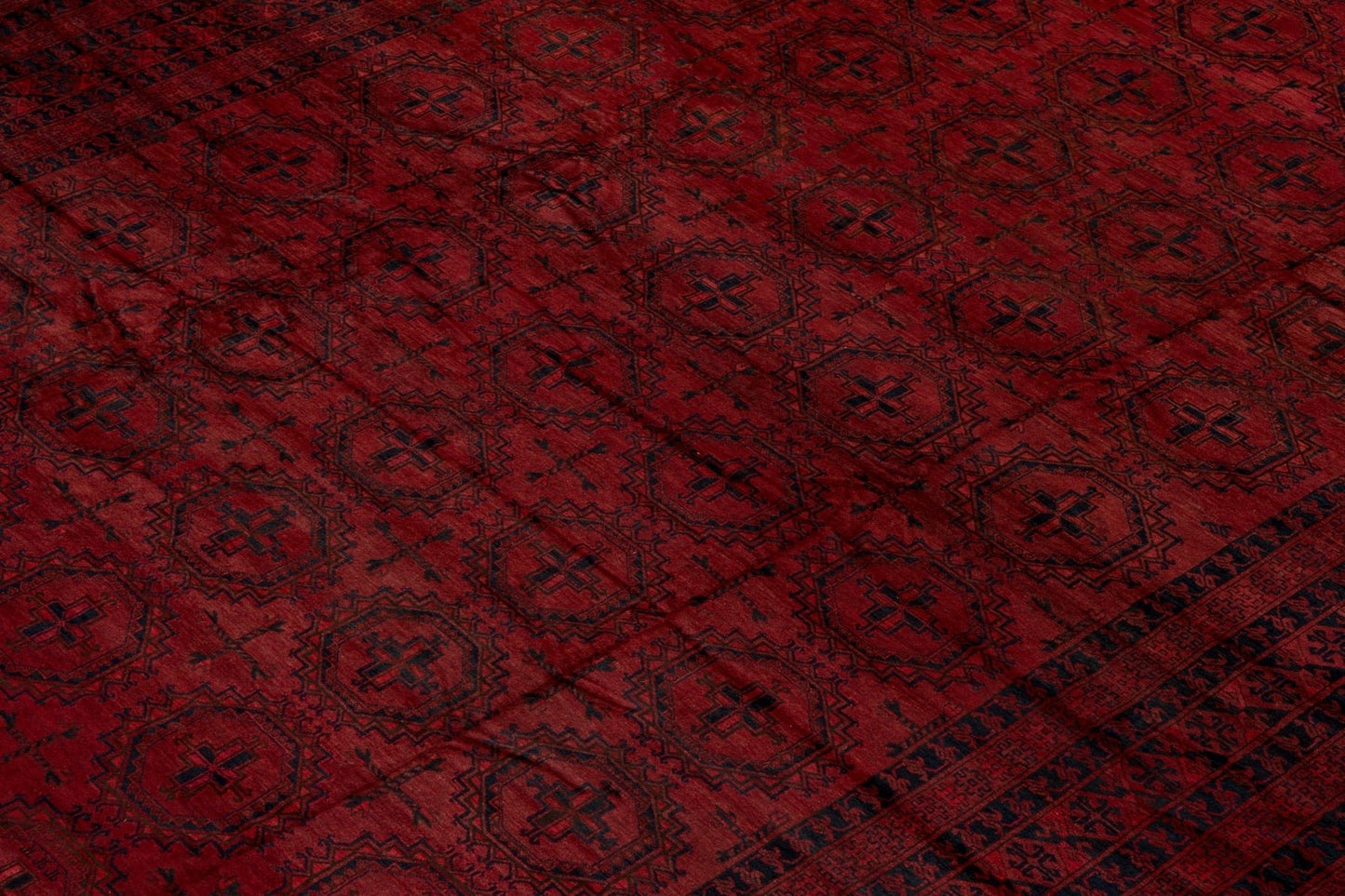 An antique Afghan Turkmen rug featuring a deep red field with repeating dark geometric motifs.