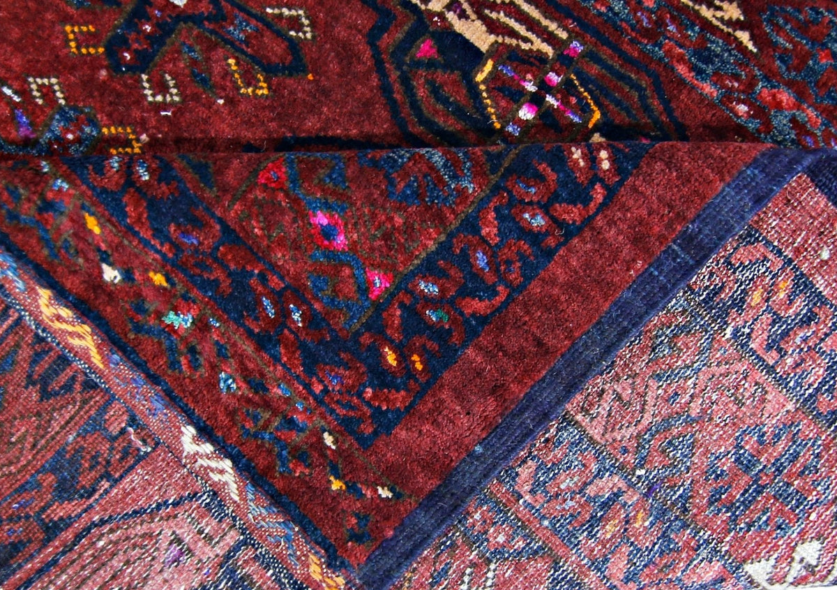 Close-up of an antique Turkmen Tekke rug showing deep red and blue geometric gul patterns and the worn wool texture.