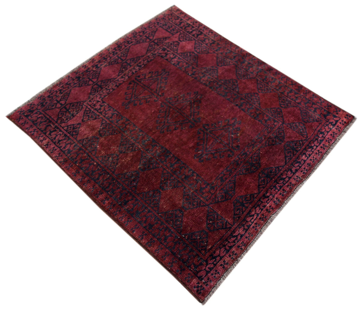 Antique Turkmen Yomut rug in deep red with dark geometric guls and intricate borders, shown from an angled perspective.