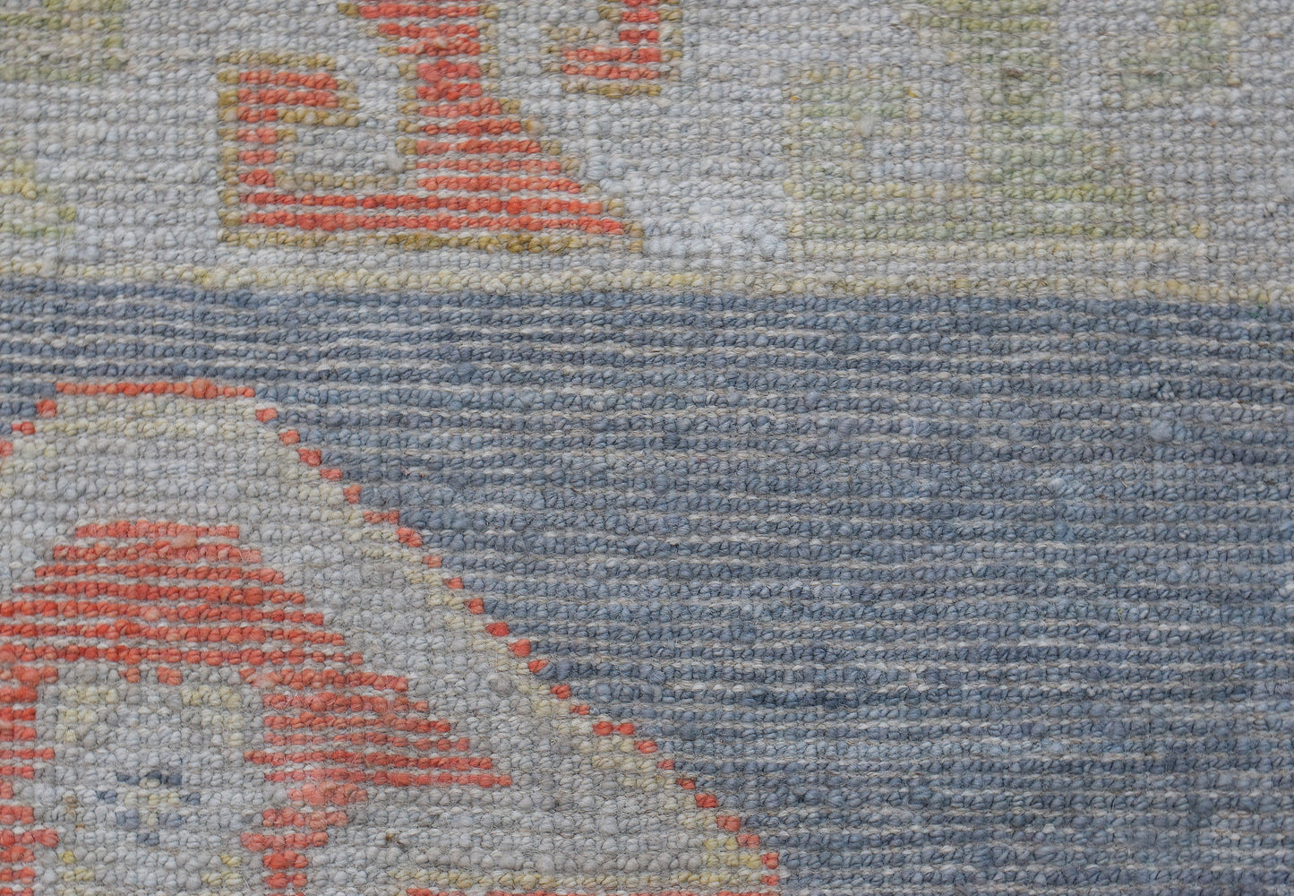 A close-up of a handwoven wool runner featuring a transitional Oushak pattern in blue and orange.