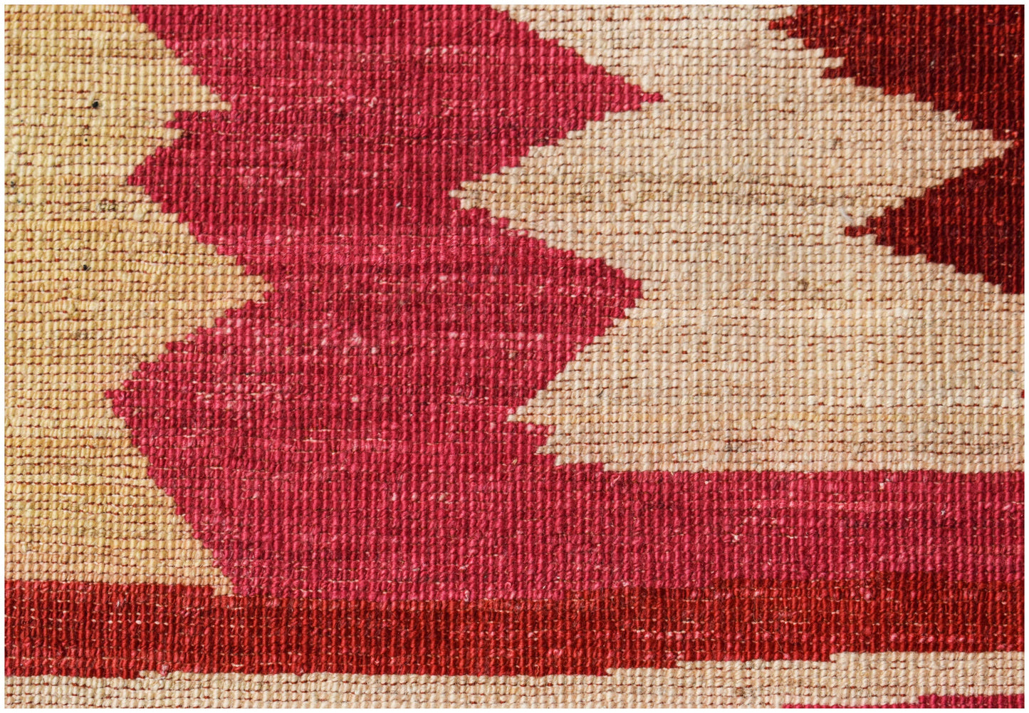 A close-up of a handmade Afghan Gabbeh rug featuring bold geometric patterns in red and cream wool.