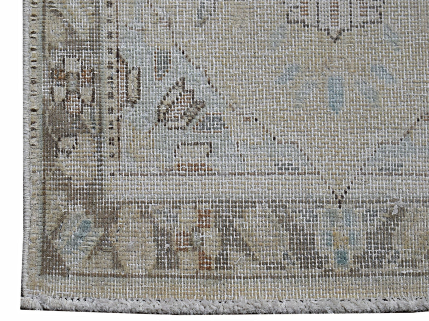 A close-up of a vintage Persian Kerman rug featuring a faded floral pattern and a fringed edge.