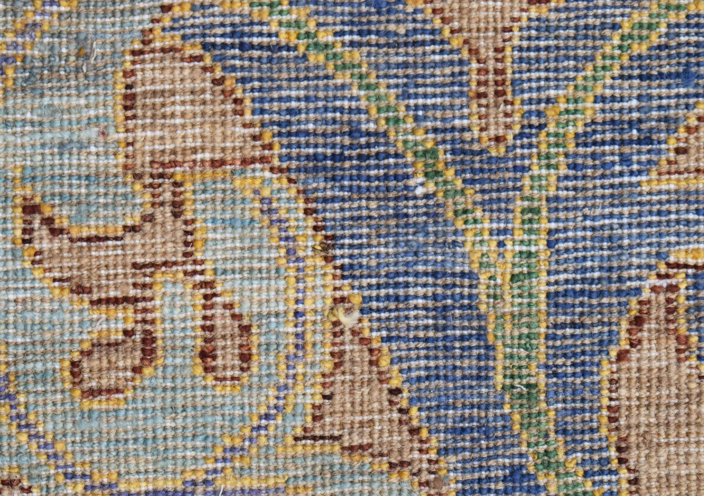 A close-up of a handwoven Afghan rug featuring a detailed floral pattern in blue, tan, and green.