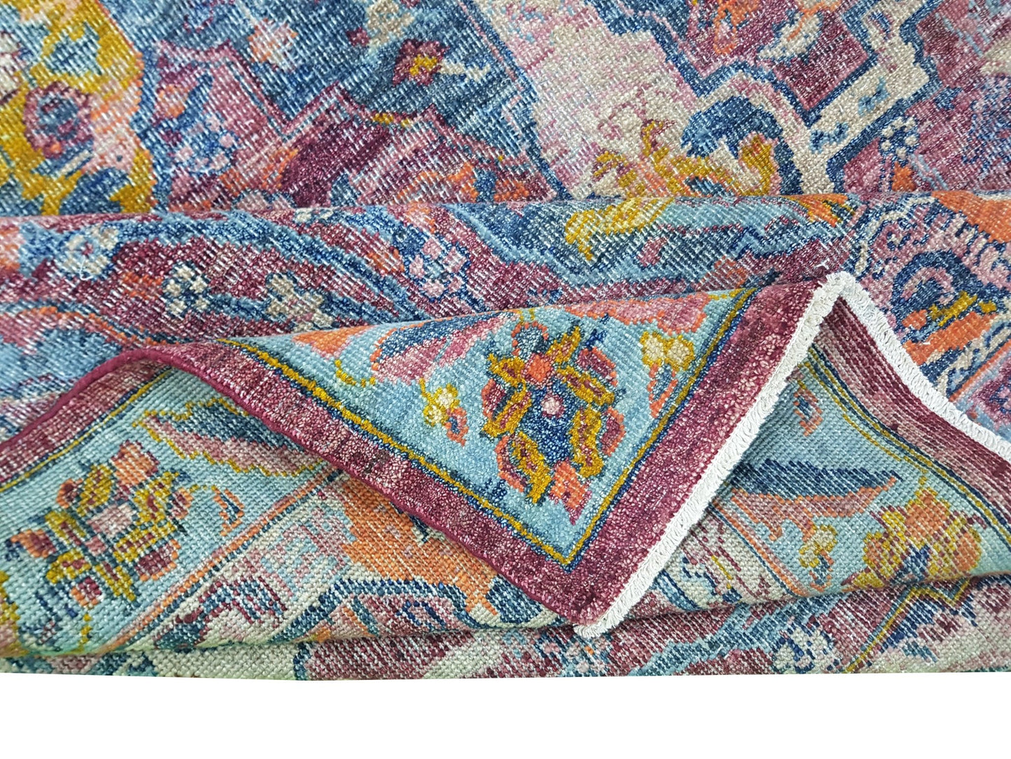 A folded transitional Afghan rug featuring a colorful floral pattern in blue, pink, and orange.