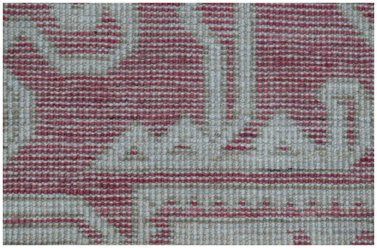 A close-up view of a handmade wool rug featuring a geometric pattern in shades of pink and cream.