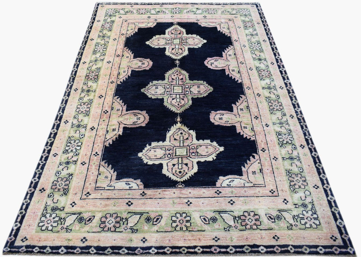 A handmade wool rug featuring a dark blue field with pink and green geometric floral motifs.