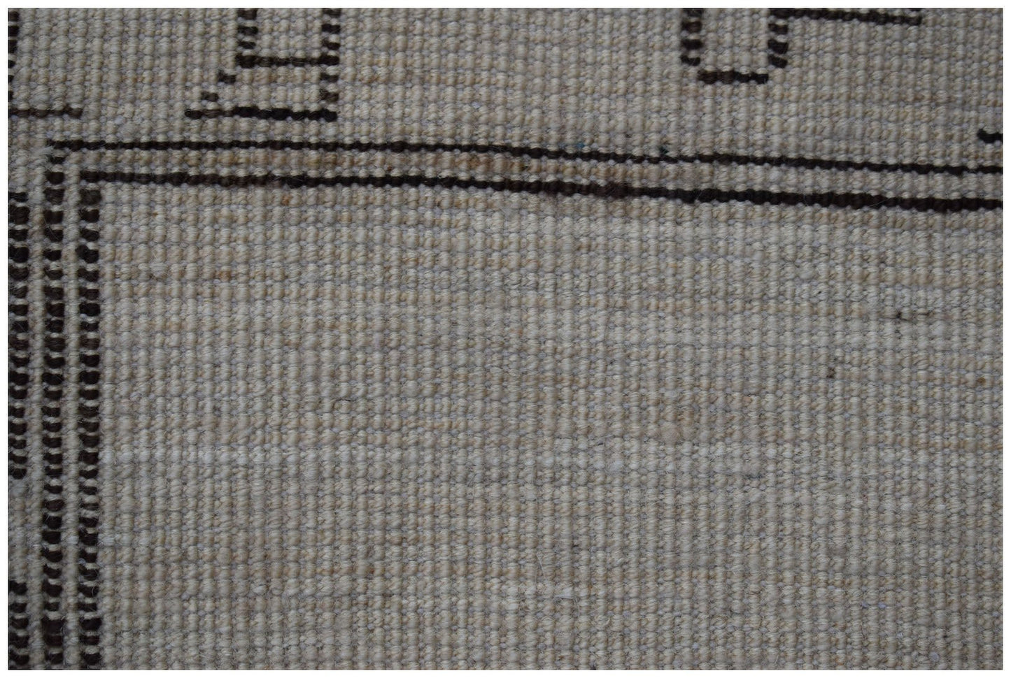 A close-up of a handmade wool rug featuring a neutral beige field with dark brown geometric borders.