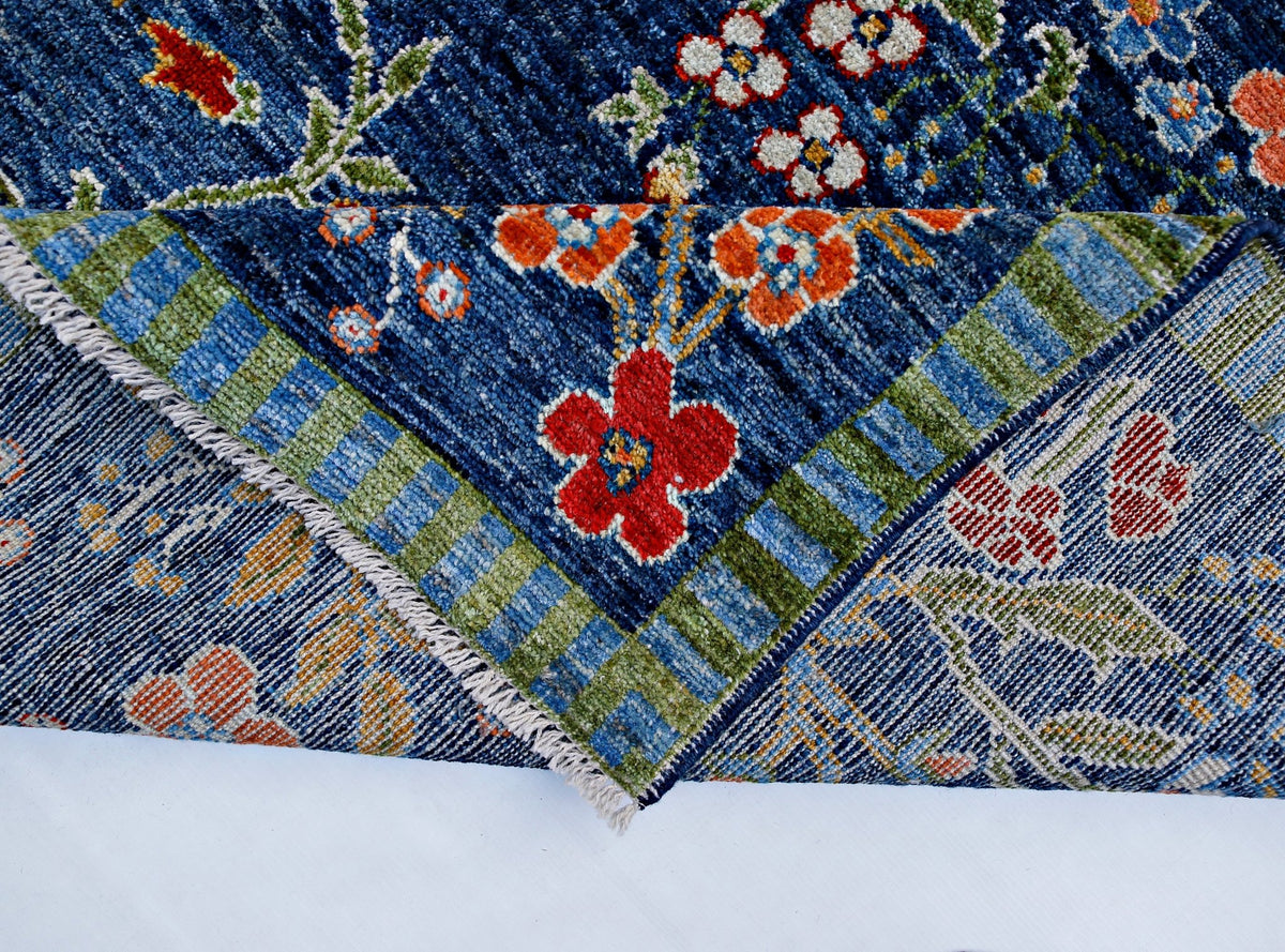 A handmade blue wool rug with a floral pattern and a green striped border, shown folded.