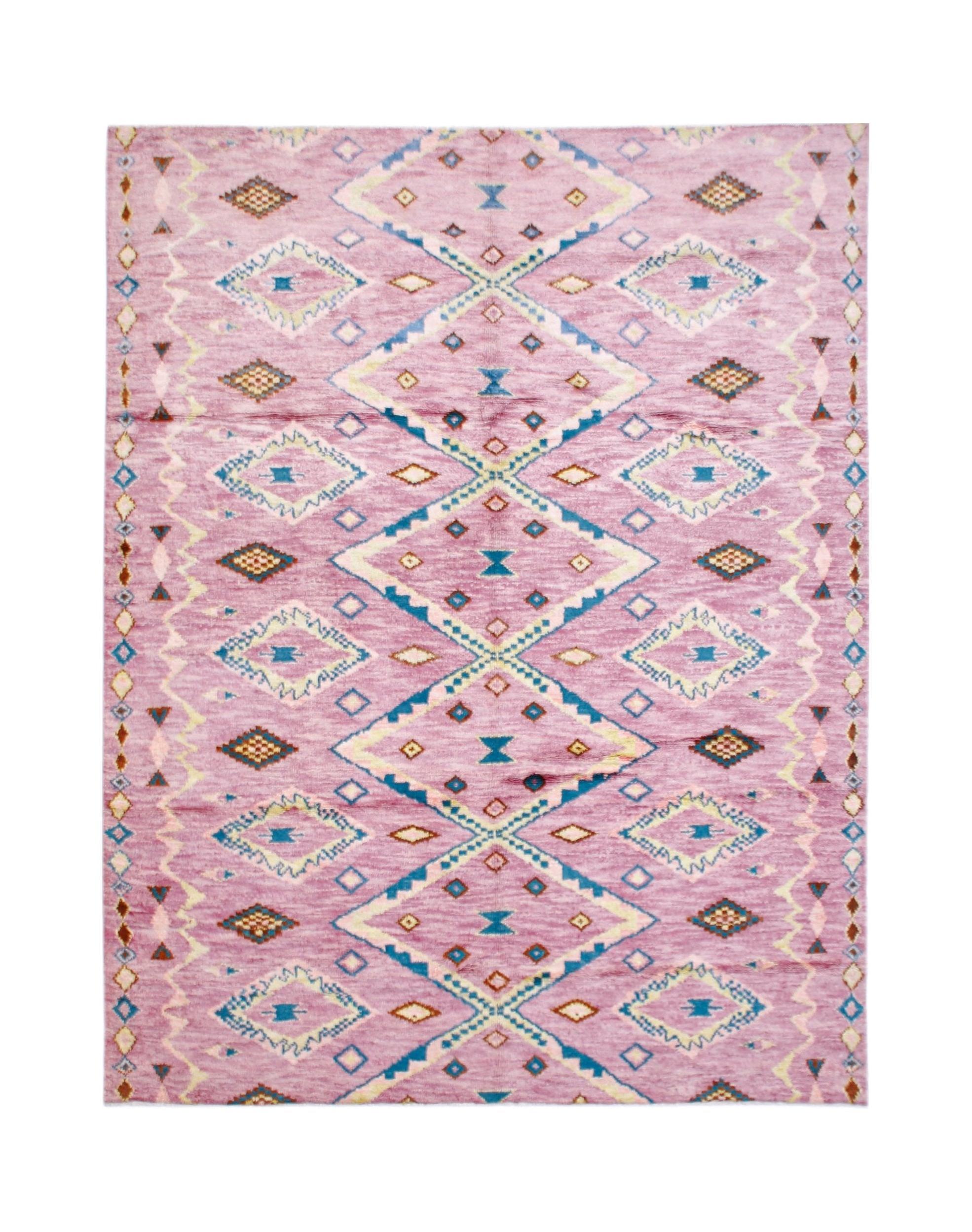 A handmade wool rug featuring a pink background with a repeating blue and cream diamond pattern.