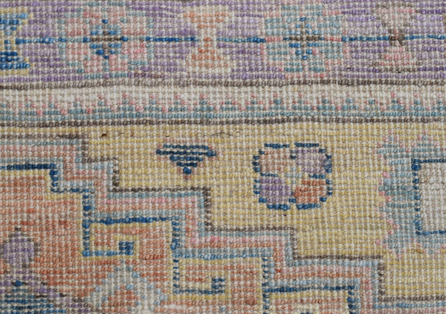 A close-up of a handwoven wool rug featuring a geometric pattern in soft pastel tones.