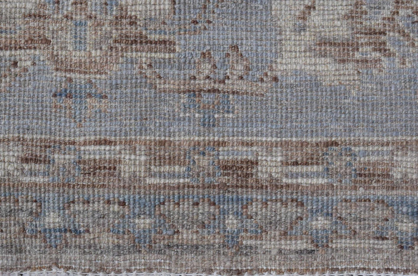 A close-up of a handwoven transitional Oushak rug featuring a textured pattern in blue and tan.