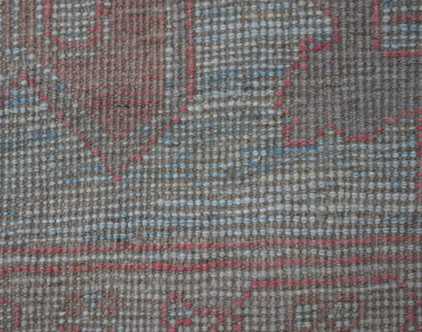 A close-up of a handwoven wool rug featuring a textured pattern in soft pink, blue, and grey tones.