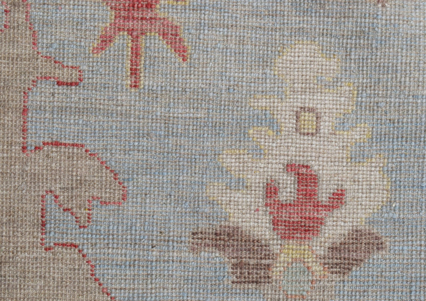 A close-up of a handwoven Oushak rug featuring a floral pattern in red, yellow, and brown tones.